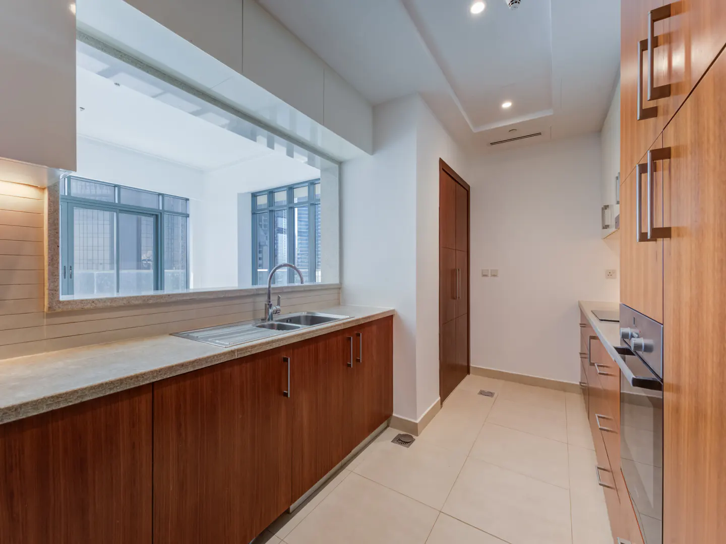 A modern kitchen with wood cabinets, stainless steel sink, and a large window overlooking a city view.