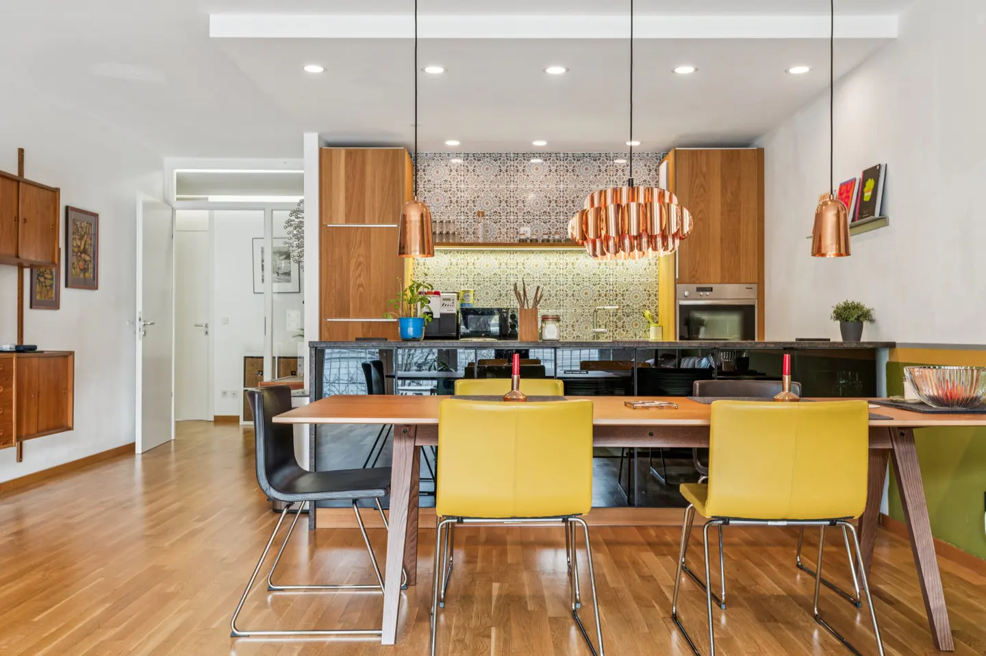 Open-concept kitchen and dining area with wood floors, yellow chairs, and copper pendant lights.