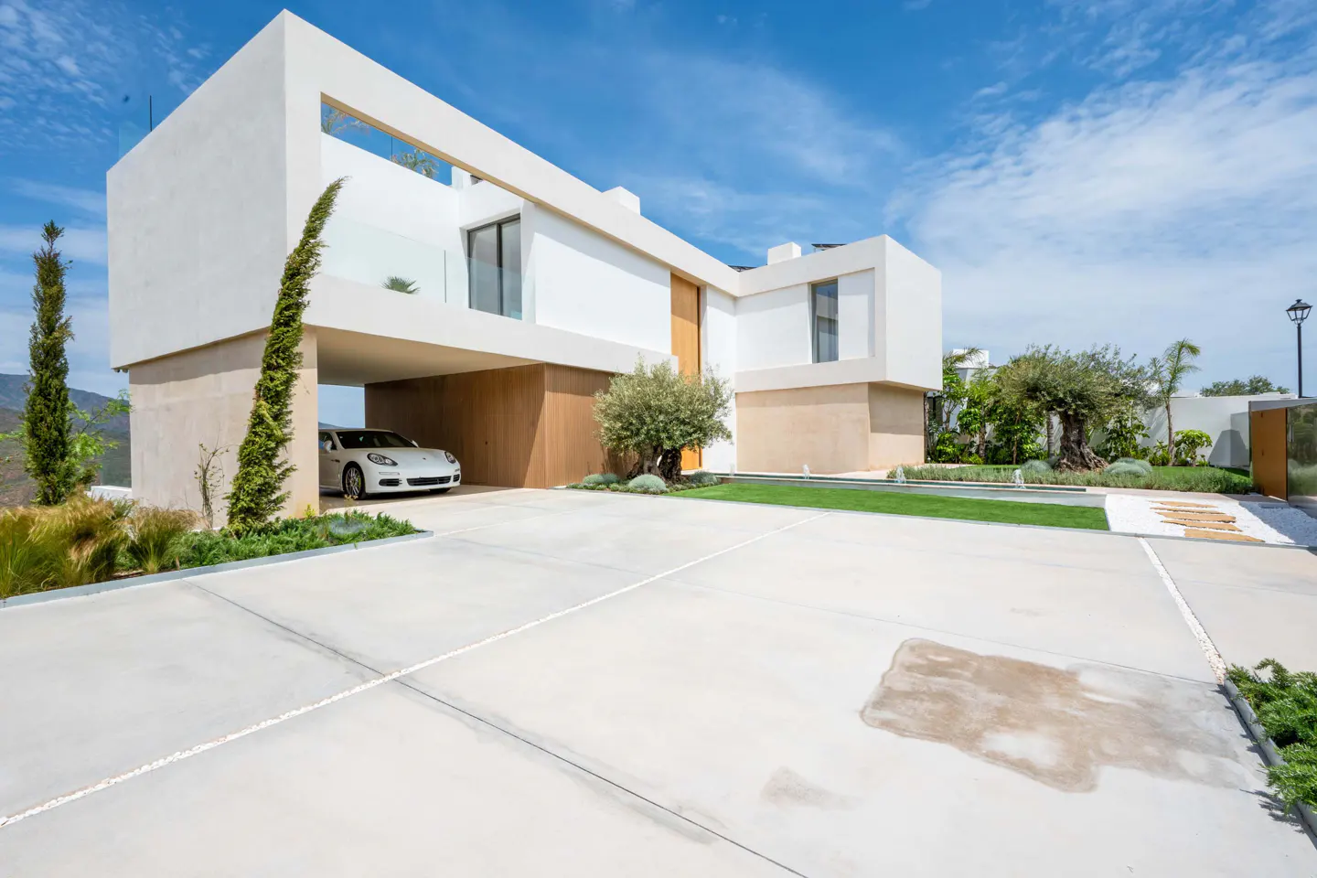 Modern white house with a car parked underneath, viewed from the driveway on a sunny day.