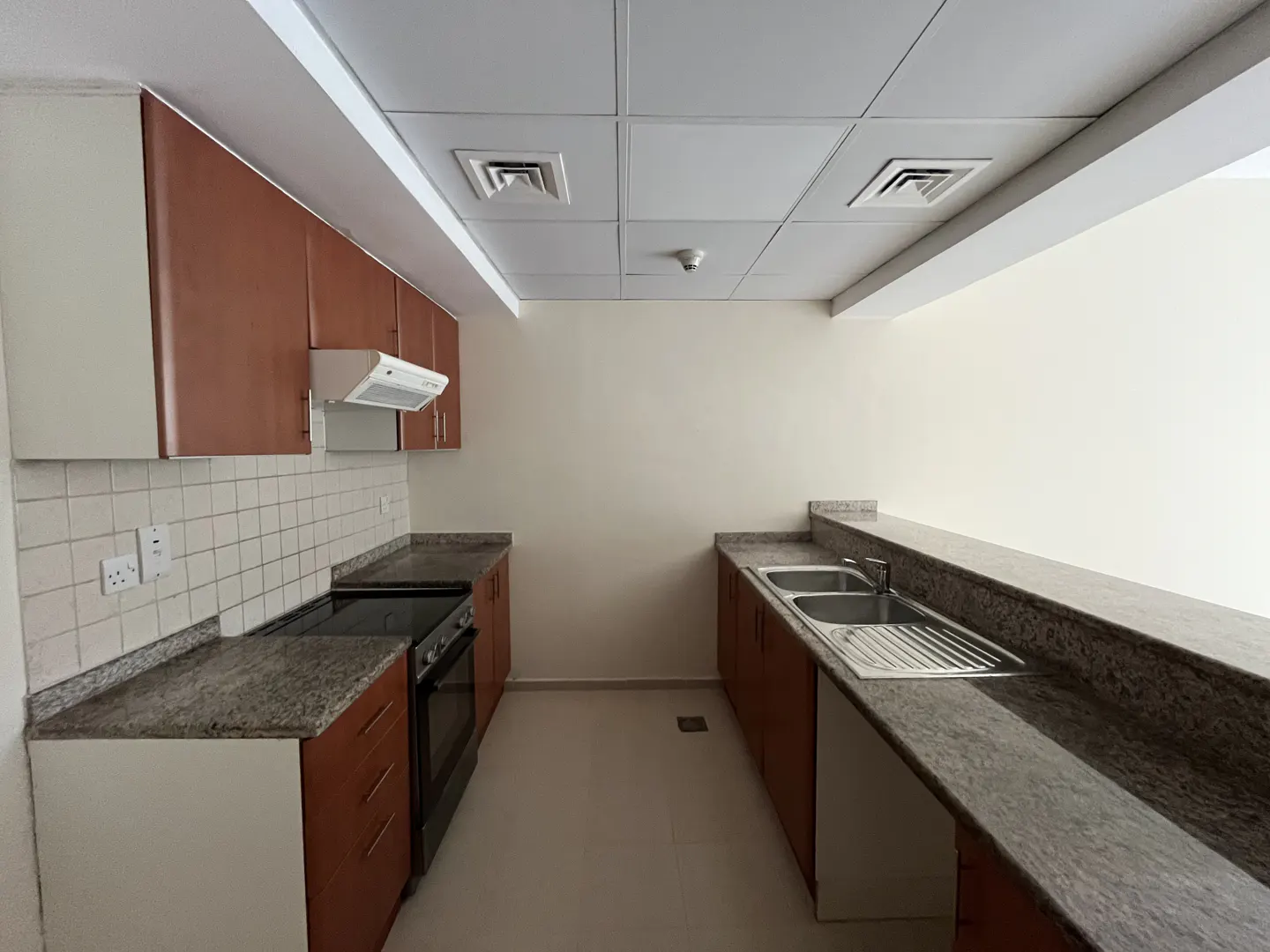 Bright kitchen with brown cabinets, granite countertops, and white tiled backsplash. Stainless steel sink and black oven.