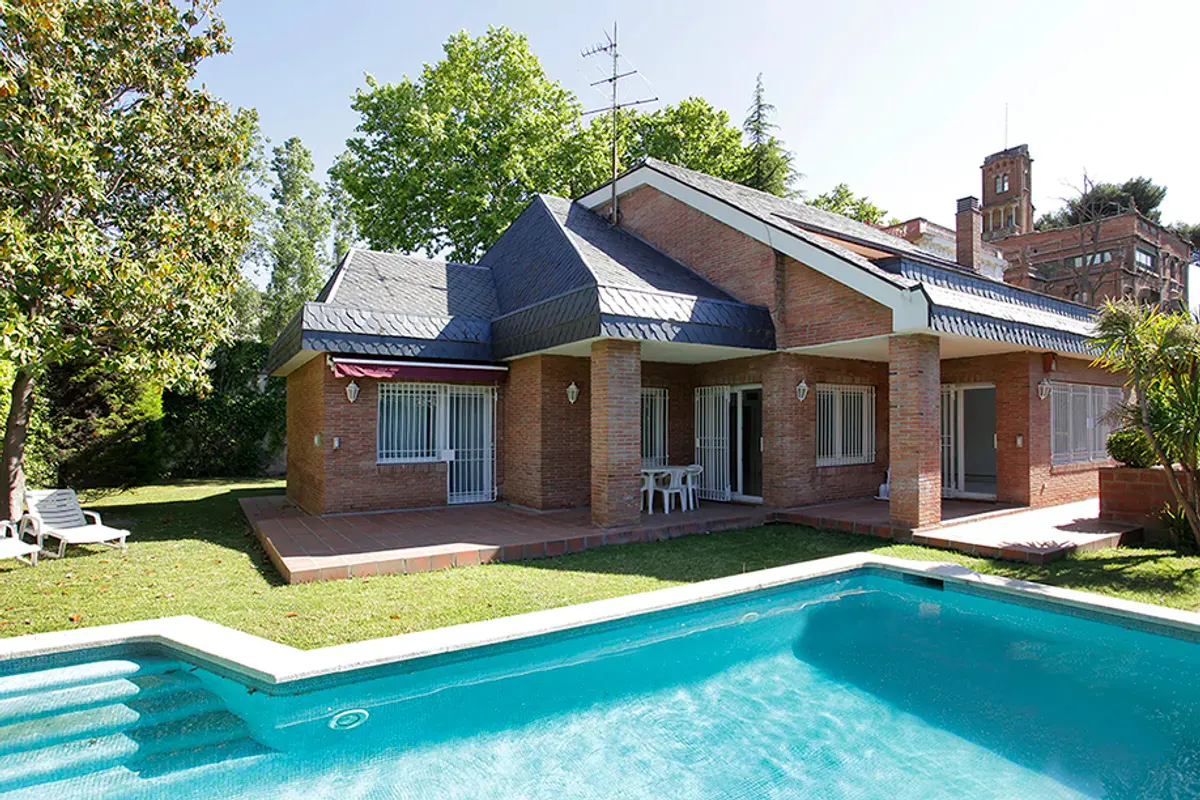 Brick house with a blue slate roof, a red awning, and a turquoise pool in the front yard.