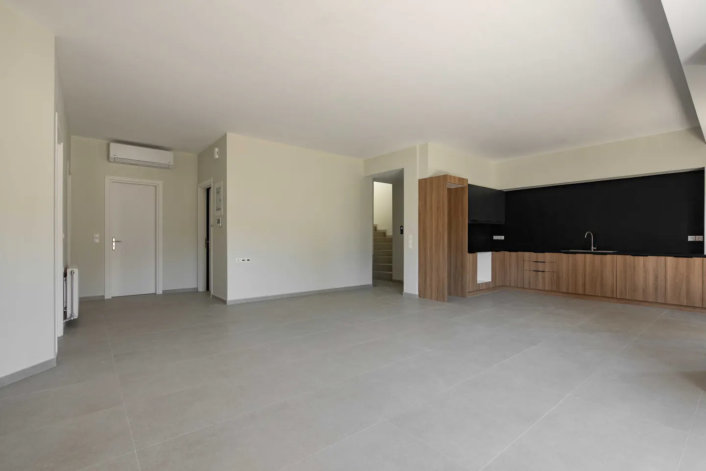 An open-concept living space with gray tile floors, white walls, and a modern kitchen with wood cabinets and a black backsplash.