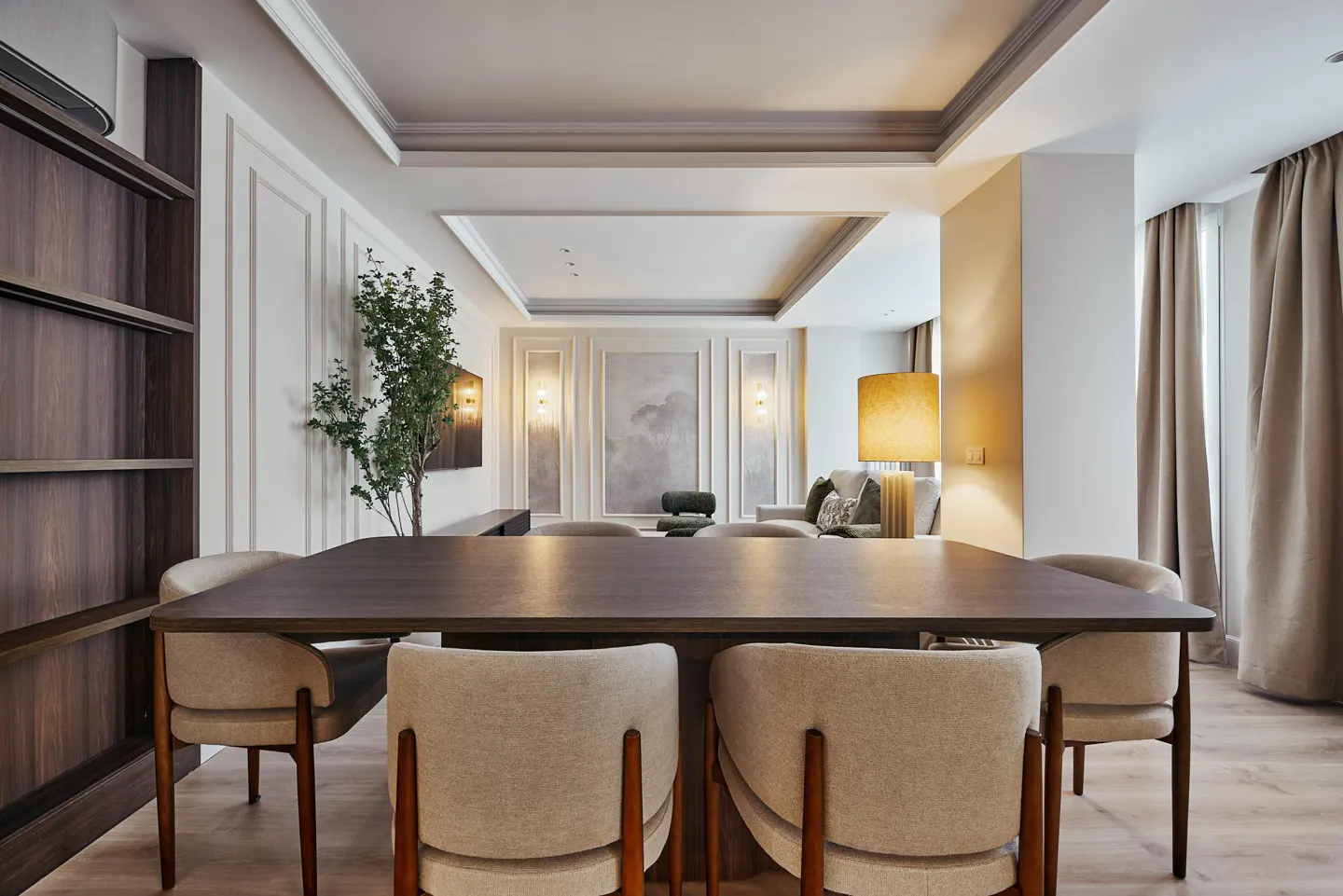 Modern dining room with a dark wood table, four beige upholstered chairs, a tall indoor plant, and elegant wall molding.