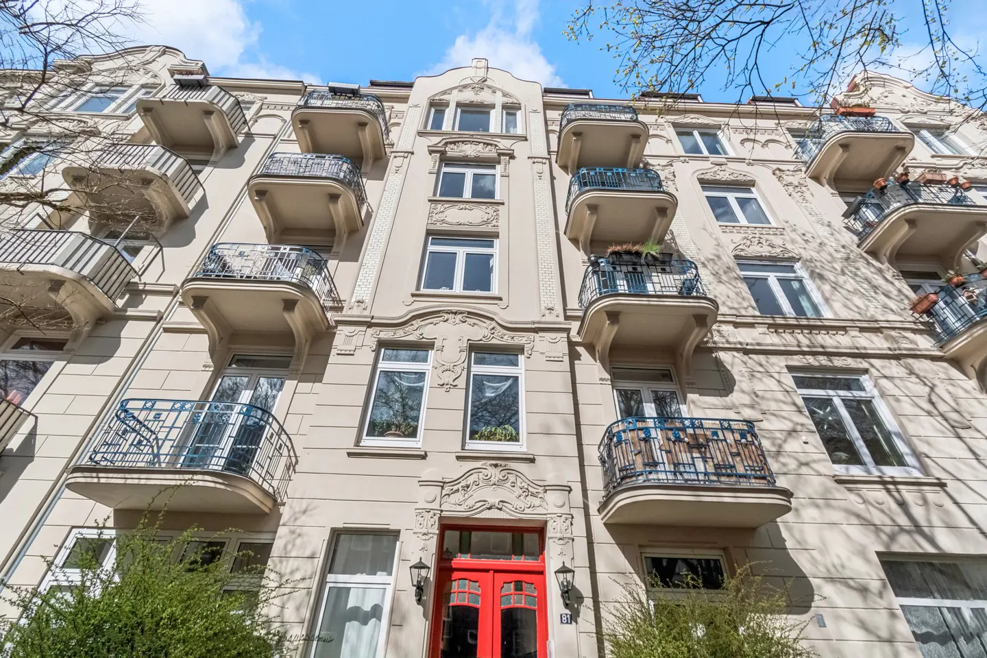 Low angle view of a beige apartment building with balconies and a red door under a blue sky.