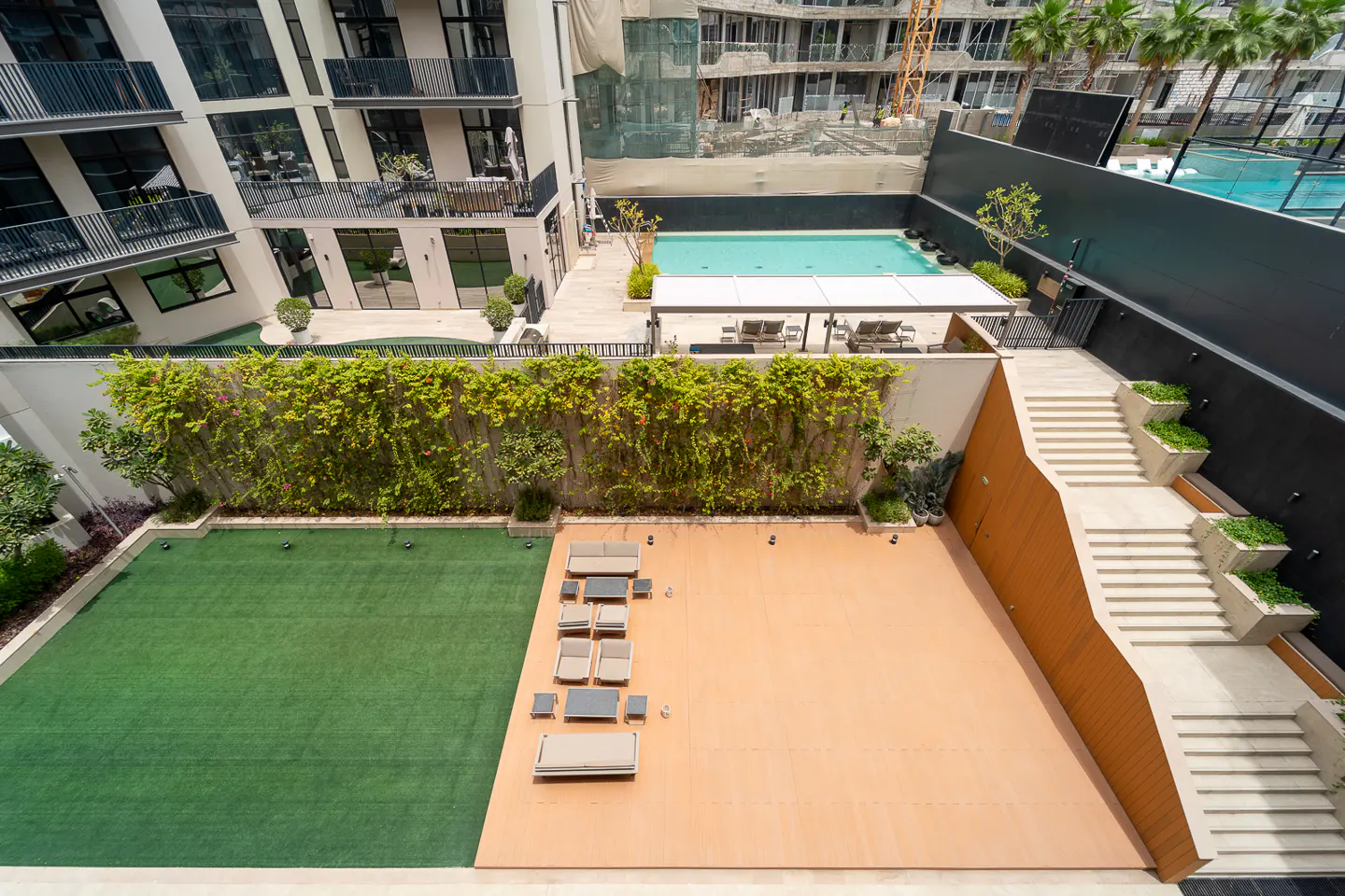 Aerial view of a building's outdoor space with a pool, lawn, patio furniture, and stairs with planters.