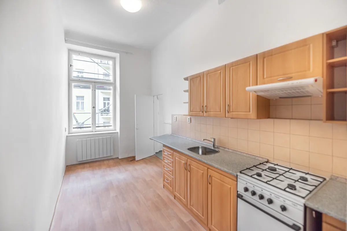 Bright kitchen with wood cabinets, gray countertops, and a white gas stove. A window overlooks a building.