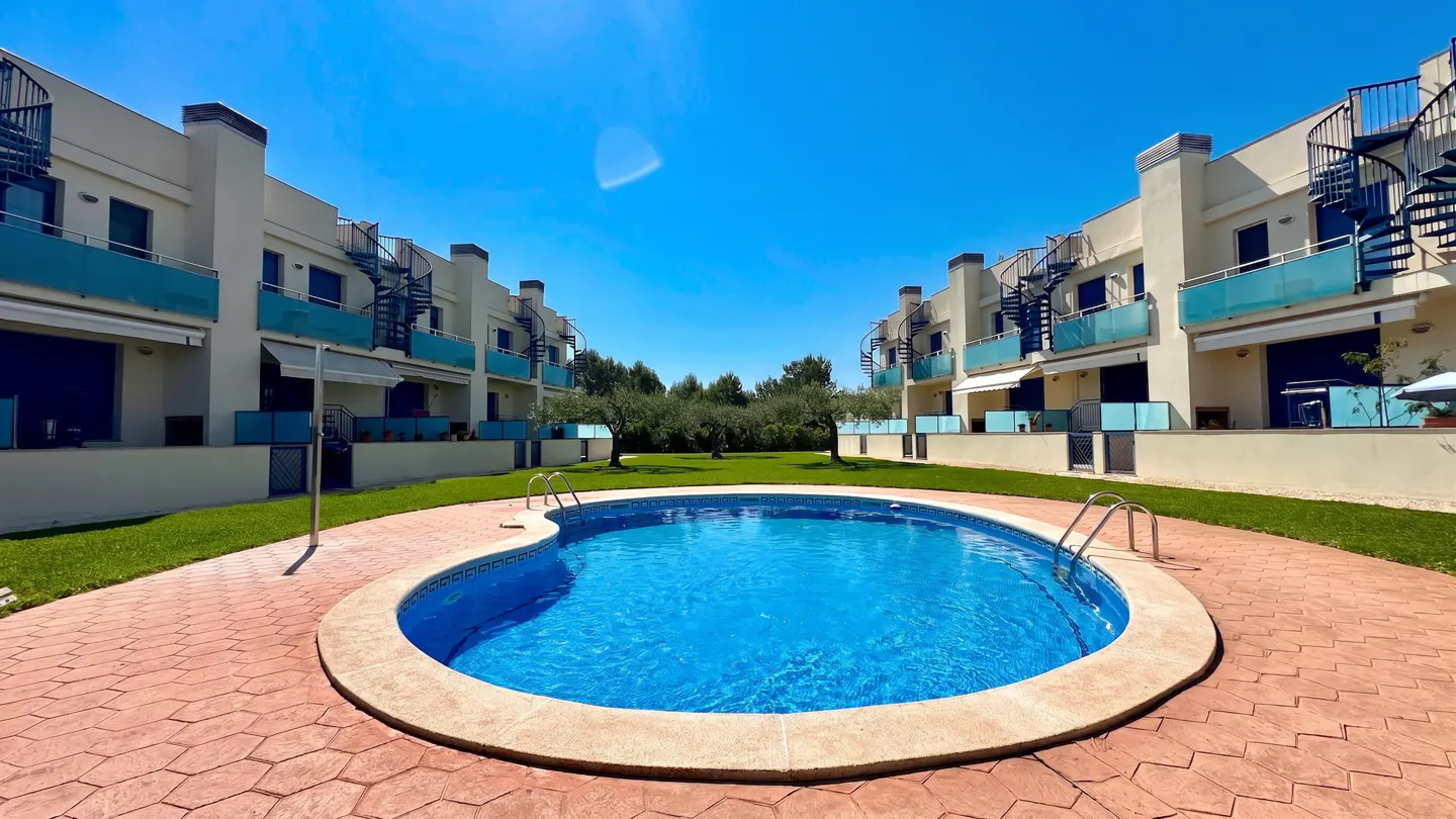 Exterior view of a blue swimming pool surrounded by beige condos with blue balconies and spiral staircases.