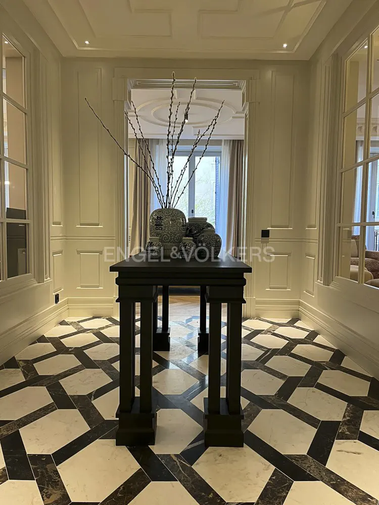Elegant foyer with black table holding vases, set against a black and white geometric tile floor. Creamy white paneled walls and doorway.