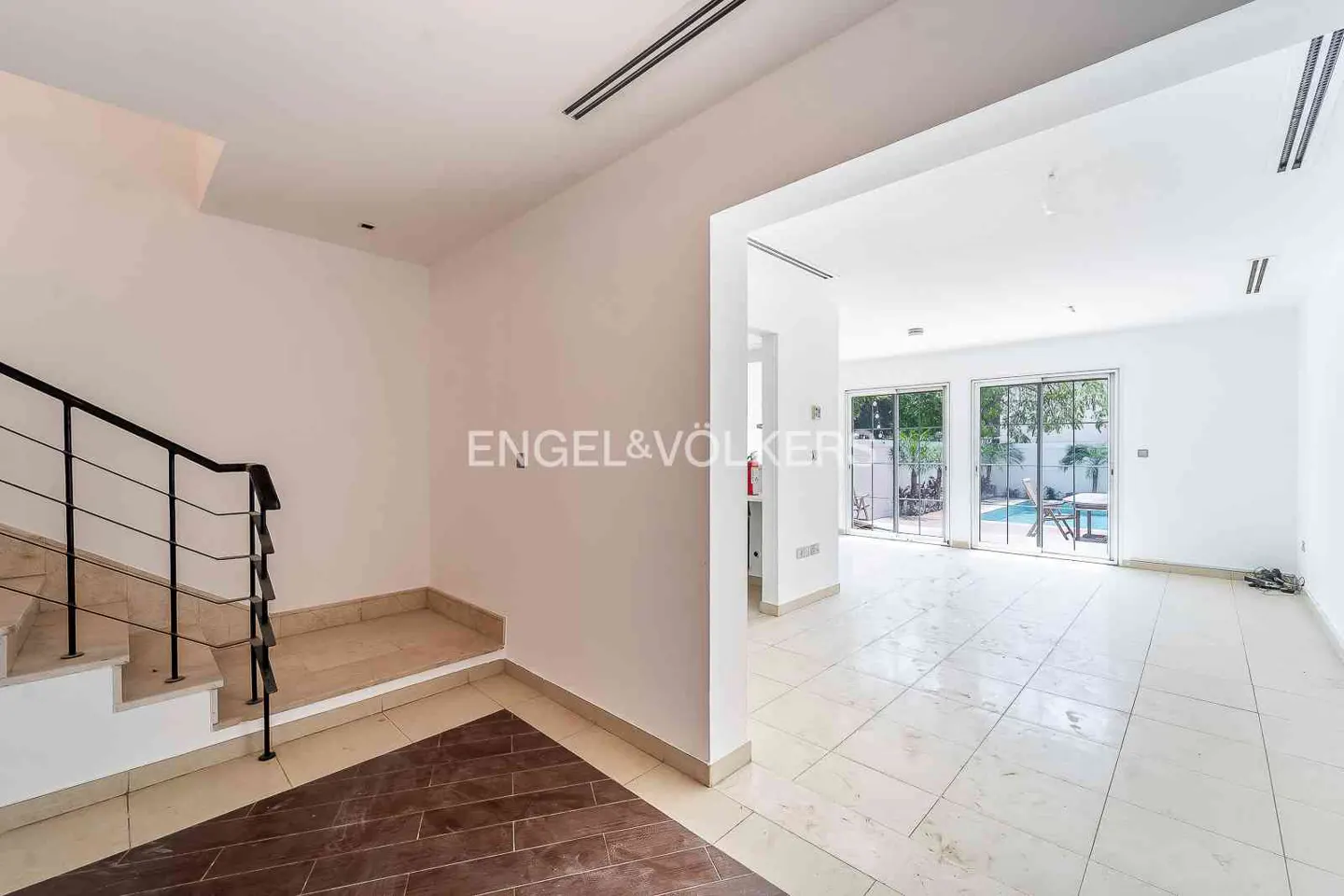 Interior view of a bright, white-walled home with stairs and a glimpse of a pool through sliding glass doors.