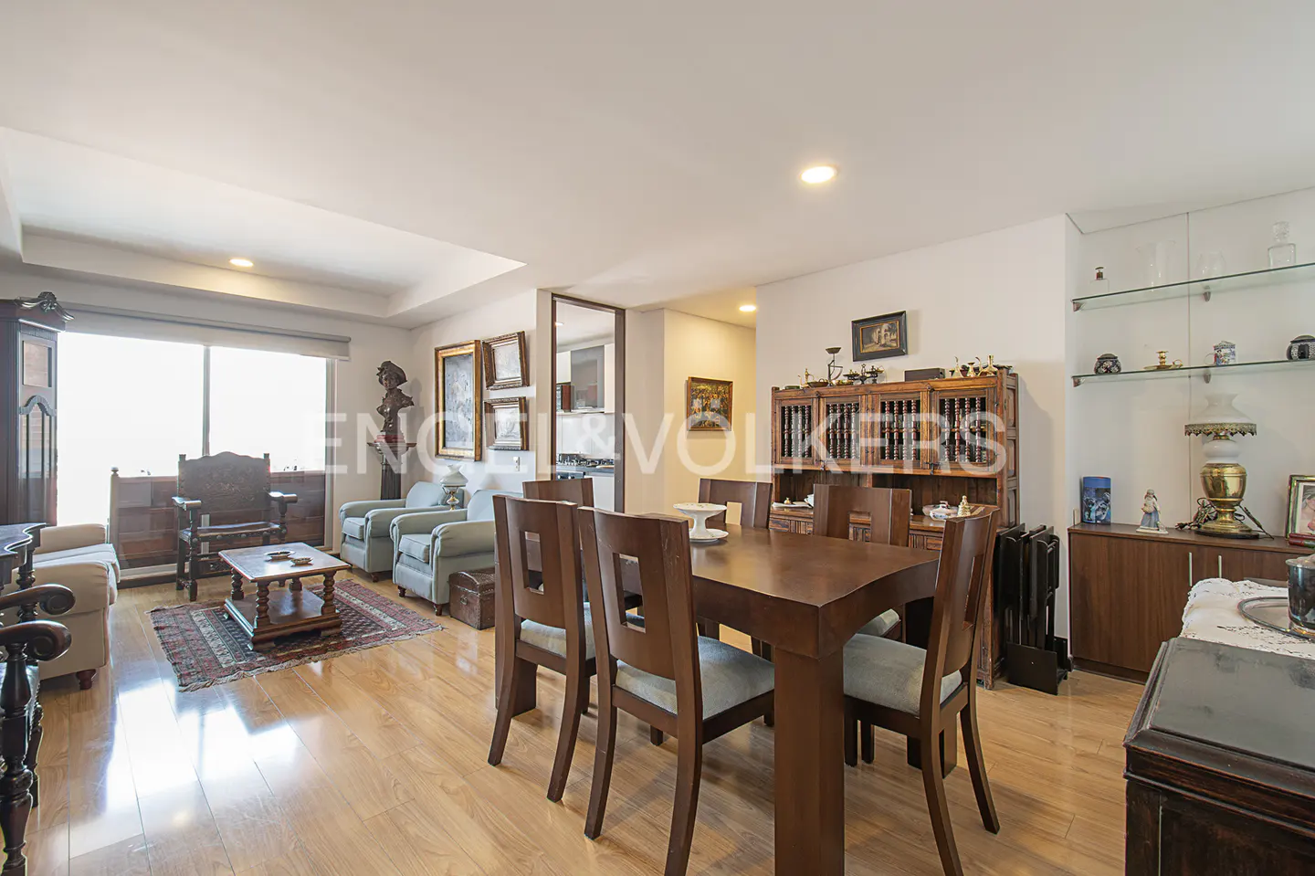 A bright living and dining area with wooden floors, a dining table with chairs, and a living room with sofas and armchairs.