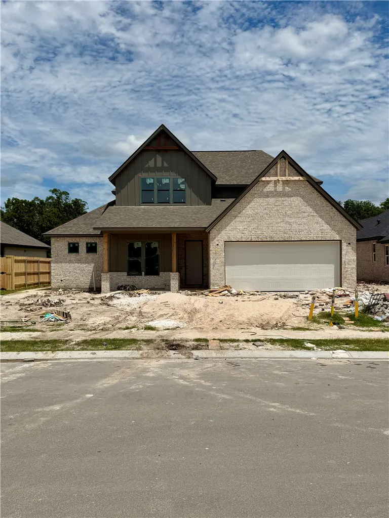 New construction home with tan brick, dark siding, and a large garage under a blue sky with scattered clouds.