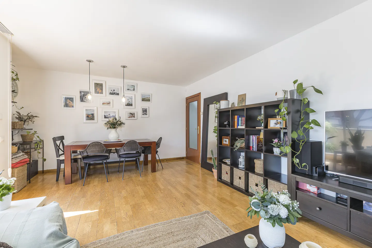 Bright living and dining room with hardwood floors, a dark wood dining set, a large black bookshelf, and a television.
