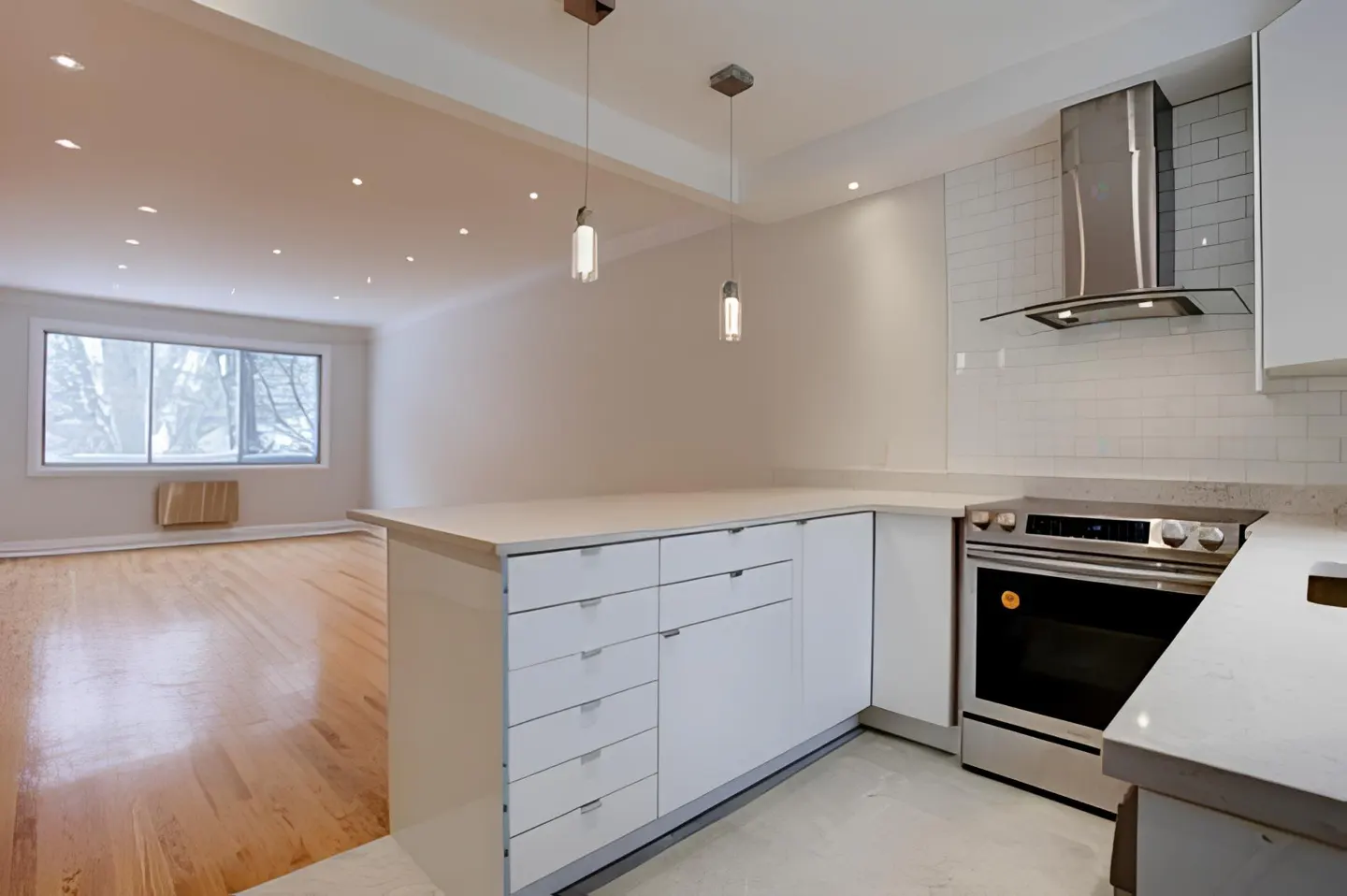 Modern kitchen with white cabinets, stainless steel stove, and subway tile backsplash, opening to a bright living area.
