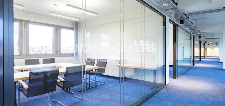 Bright office space with glass-walled conference room, blue carpet, and Engel & Völkers logo on the glass.