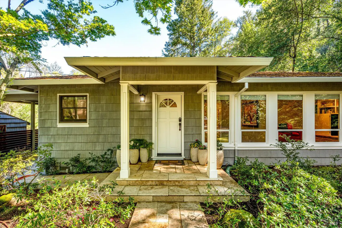Front view of a house with gray siding, a white door, and a stone walkway. Green trees surround the house.