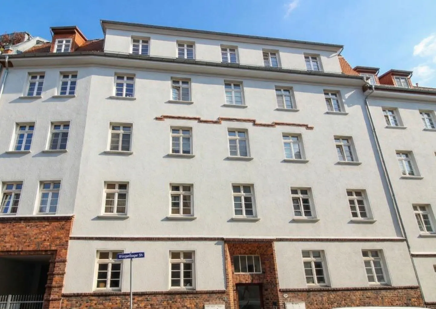 Exterior of a white, multi-story apartment building with brick accents under a blue sky.