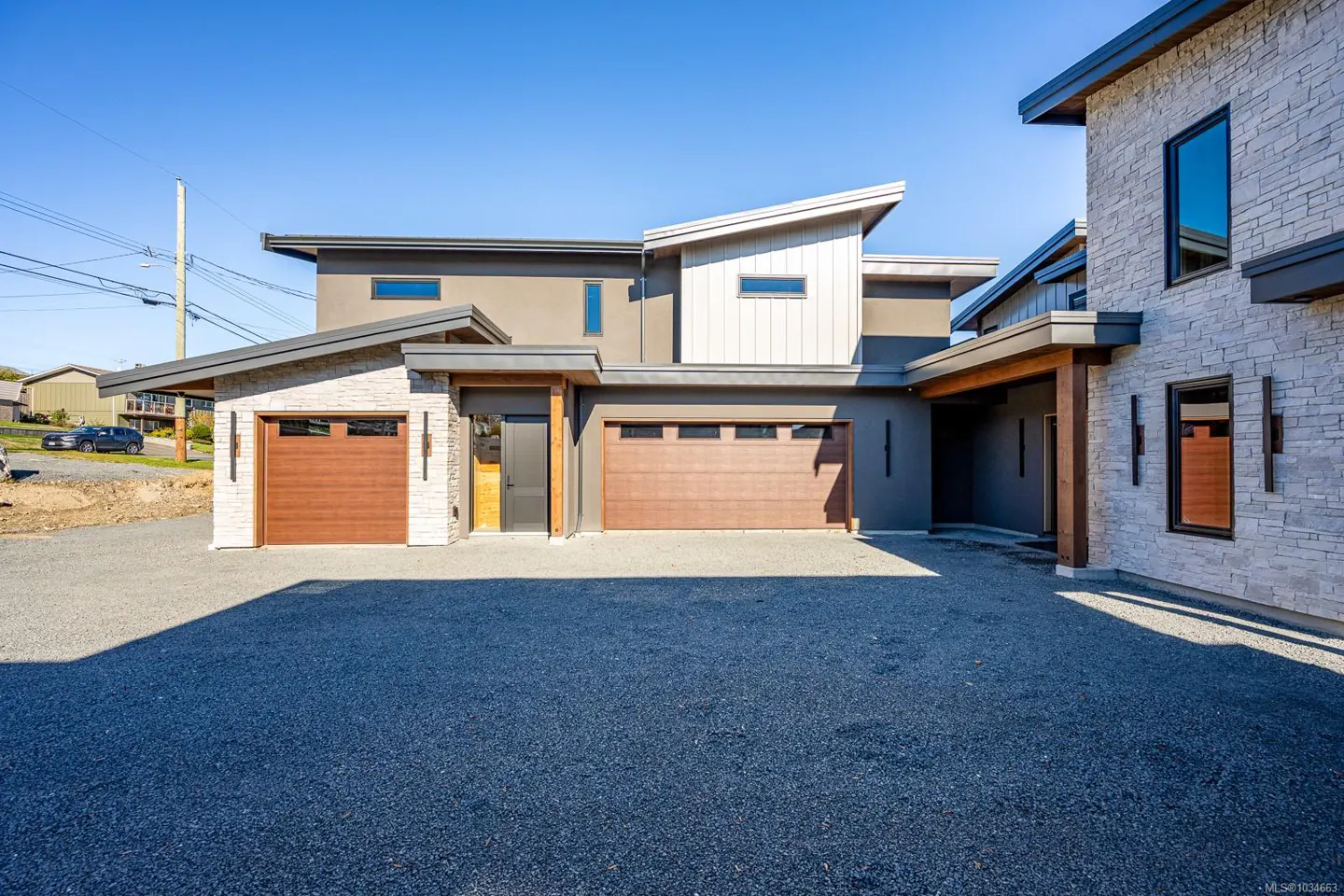 Modern home exterior with brown garage doors, stone accents, and gray siding under a clear blue sky.
