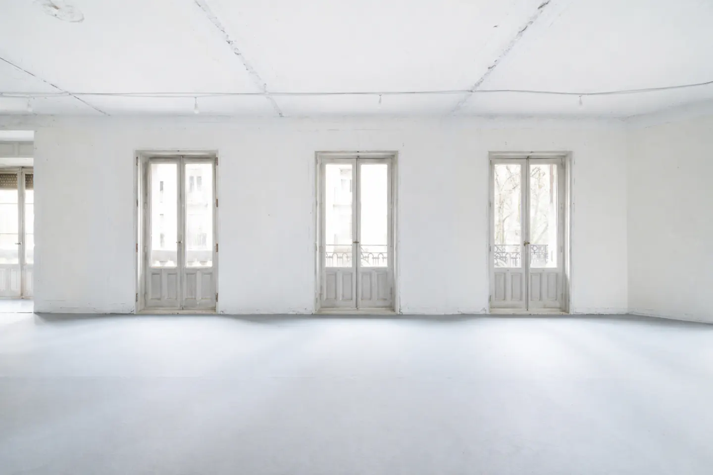 Bright, empty white room with three sets of white double doors leading to balconies.