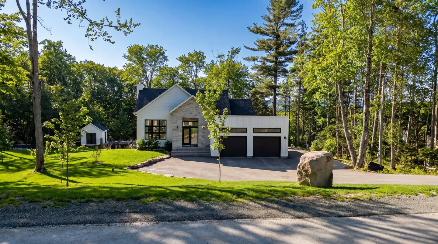 Modern white house with black garage doors and stone accents, surrounded by green trees and a blue sky.