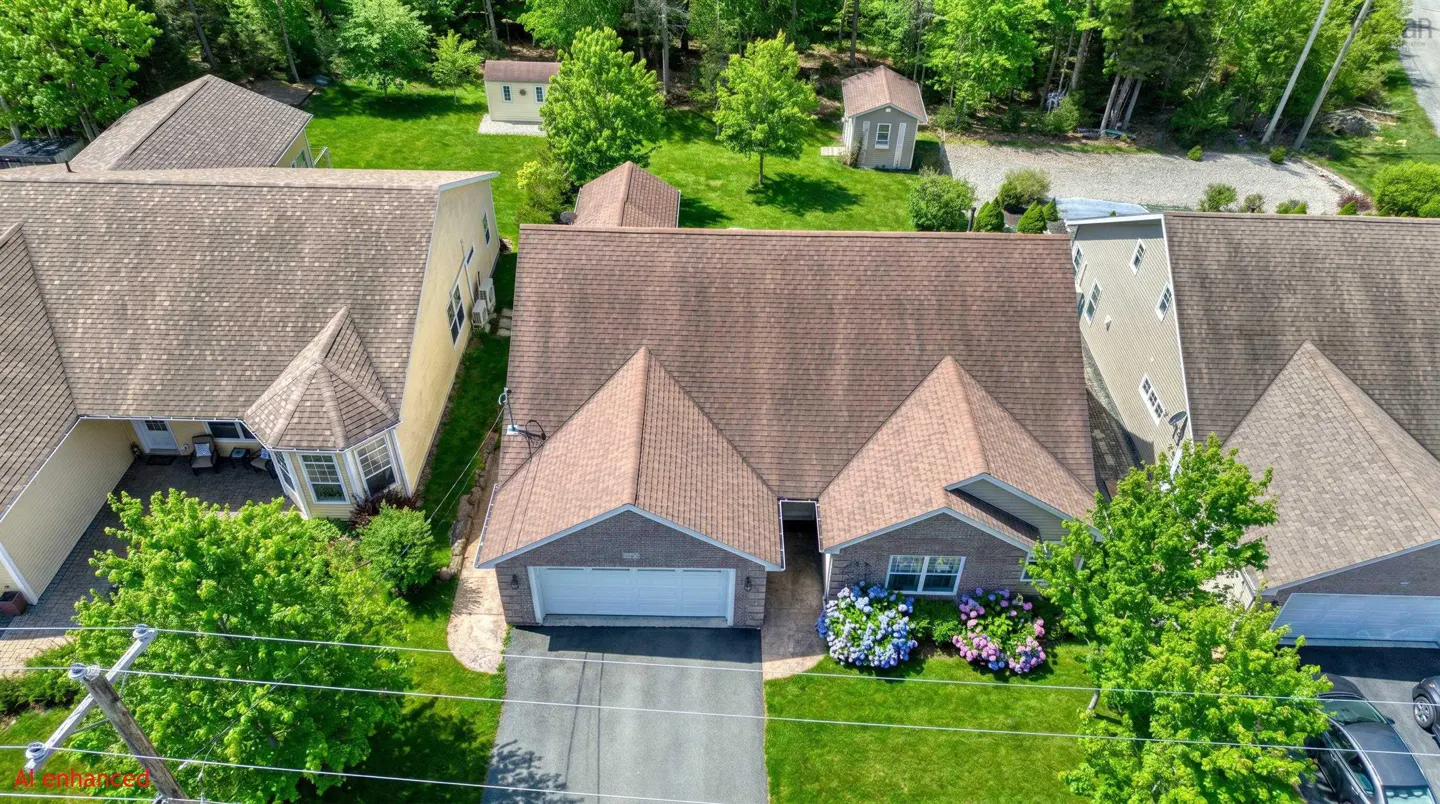 Aerial view of a brick house with a brown roof, green lawn, and blue and pink hydrangeas. Other houses and trees are in the background.
