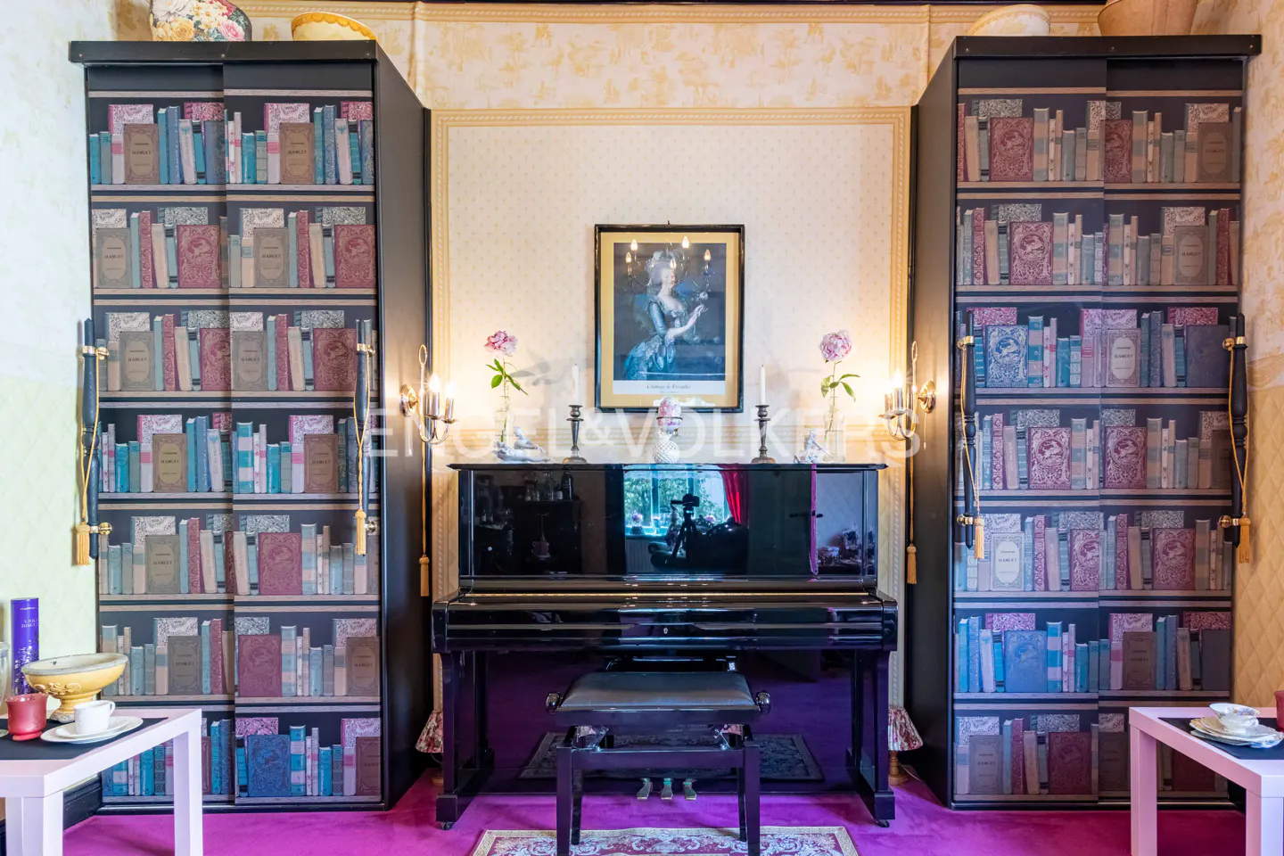 A room with a black piano, flanked by two tall cabinets with a bookshelf design. A framed portrait hangs above the piano.