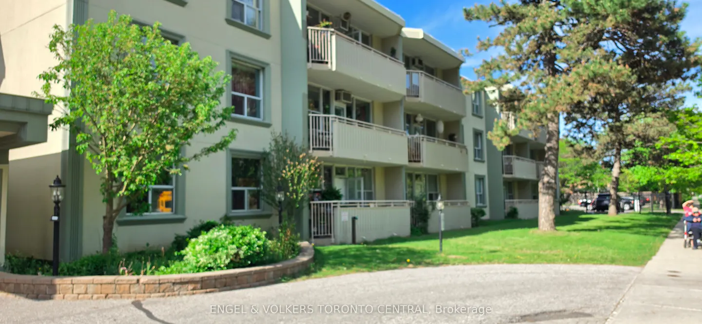 Exterior view of a light green, multi-story apartment building with white balconies and green trees.