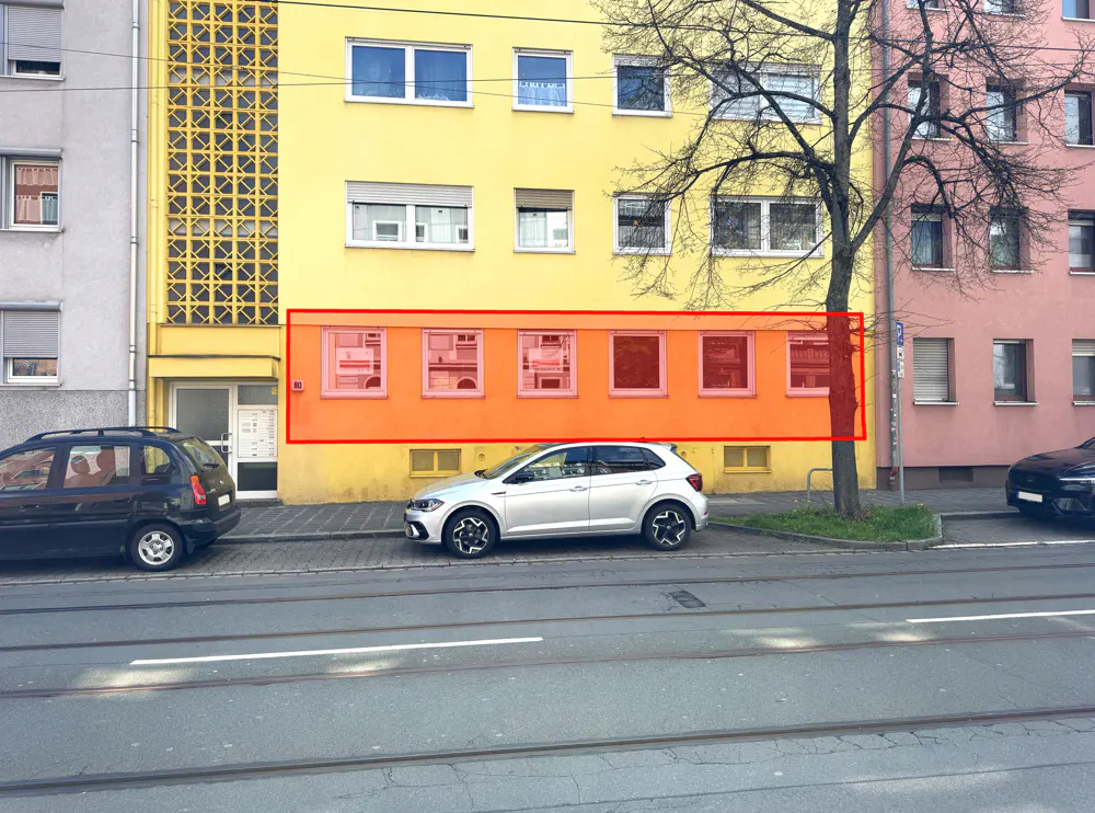 Street view of a yellow apartment building with six windows outlined in red. Cars are parked on the street.