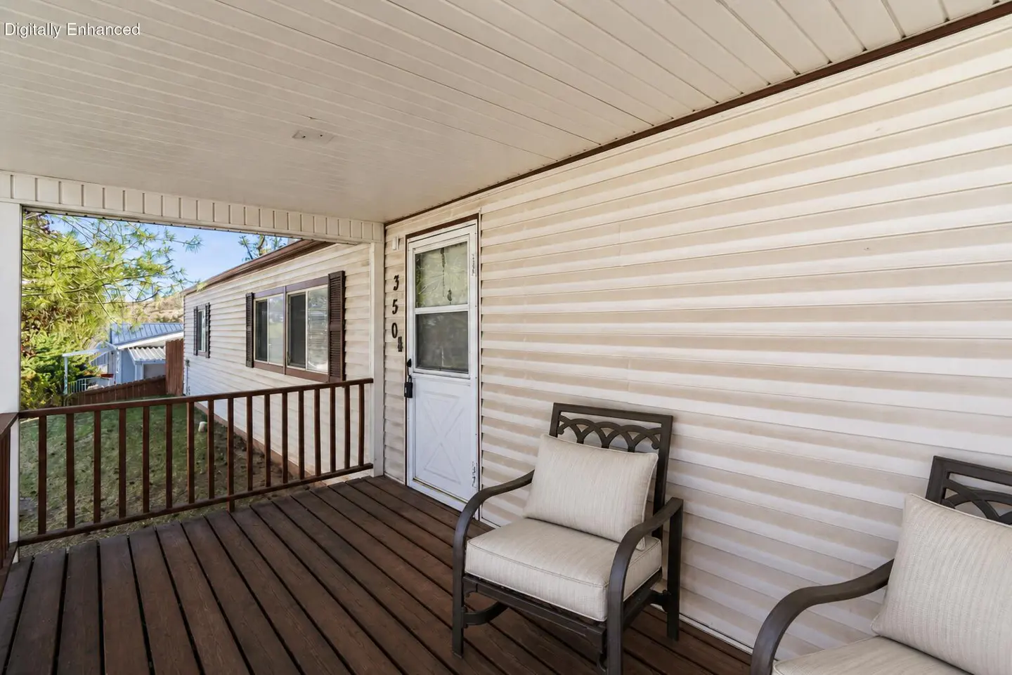 Covered porch with two chairs and a white door with the number 3504 on a beige house with brown trim.