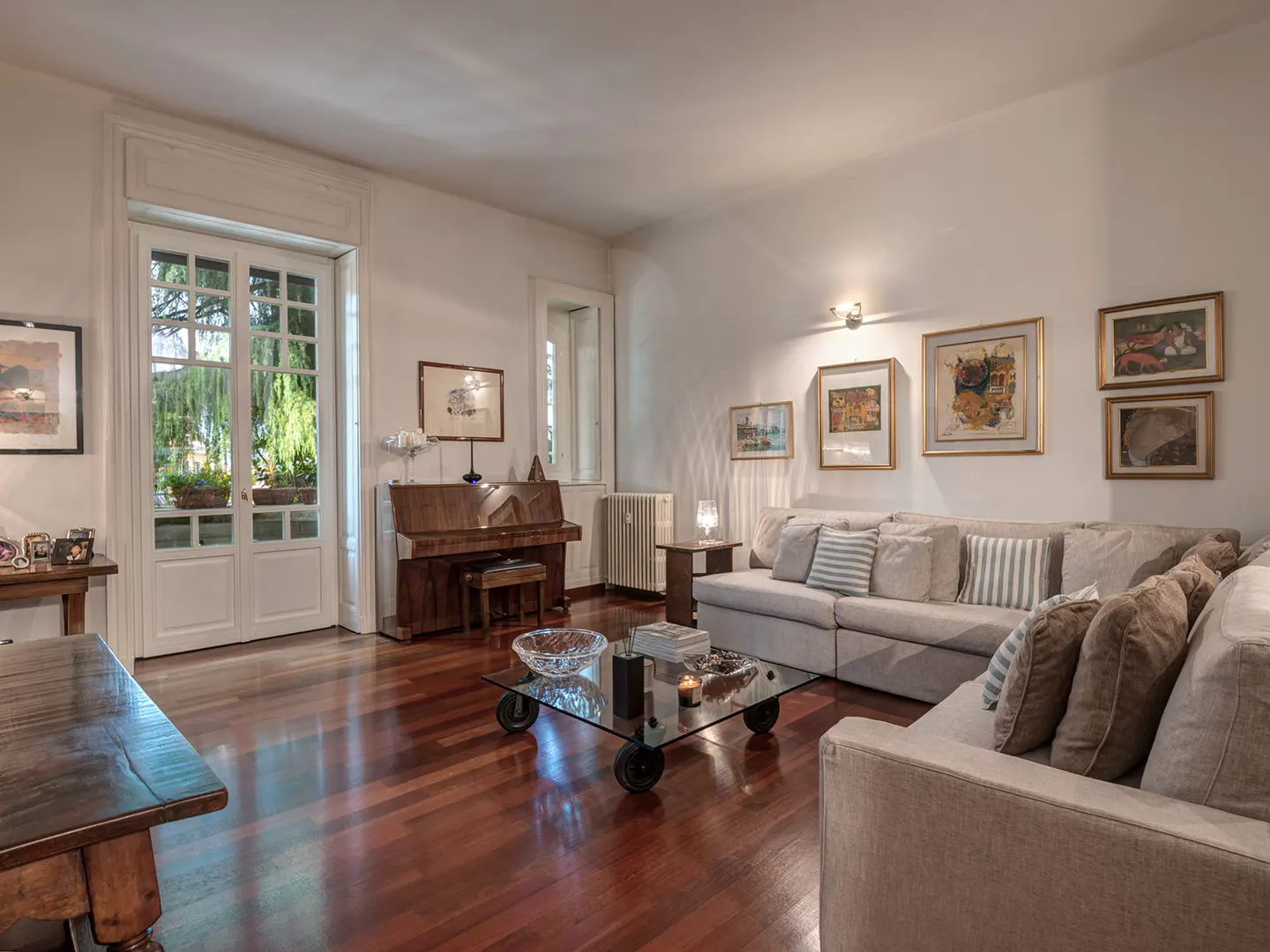 Bright living room with hardwood floors, a large beige sectional sofa, glass coffee table, and an upright piano.