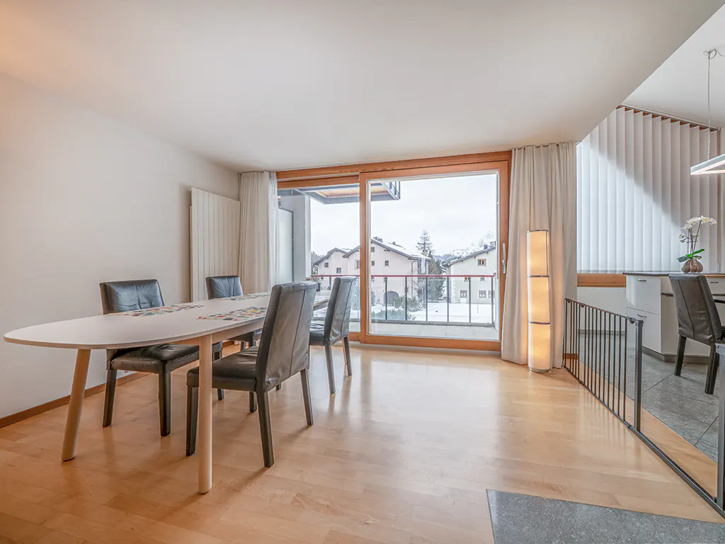 Bright dining room with wood floors, a white table with black chairs, and a sliding glass door to a balcony with a snowy view.