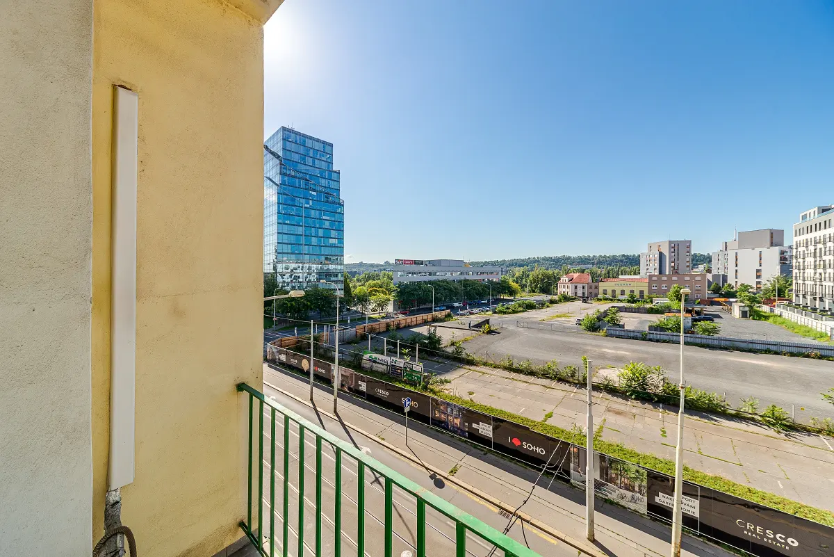 View from a balcony with green railings, overlooking a city street with a modern glass building in the background.