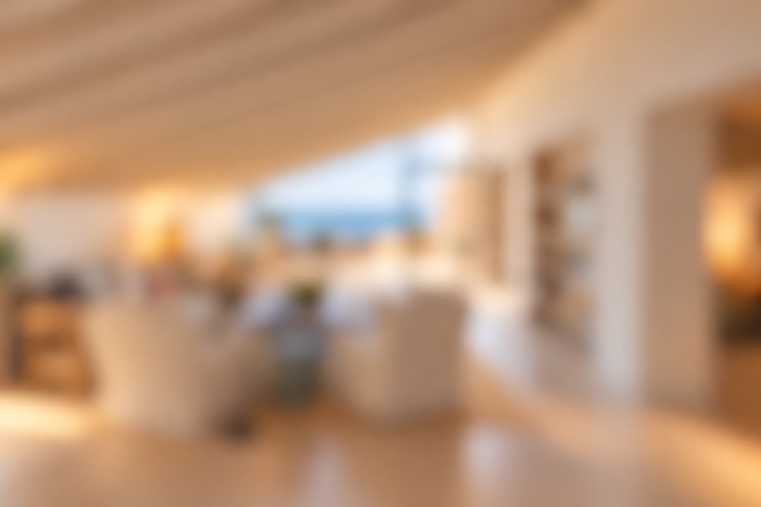 Blurred view of a bright, modern living room with white furniture and a large window overlooking a blue ocean view. [AI-generated text]