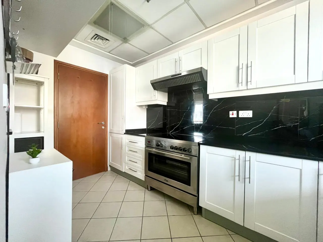 A kitchen with white cabinets, black marble countertops, and stainless steel appliances. A brown door is on the left.