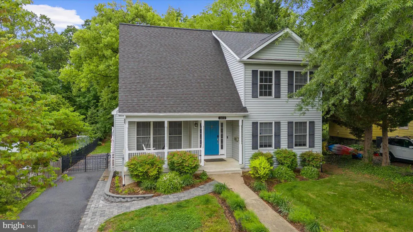 Two-story gray house with black shutters and a bright blue front door. A screened porch is on the left. Green trees surround the property.