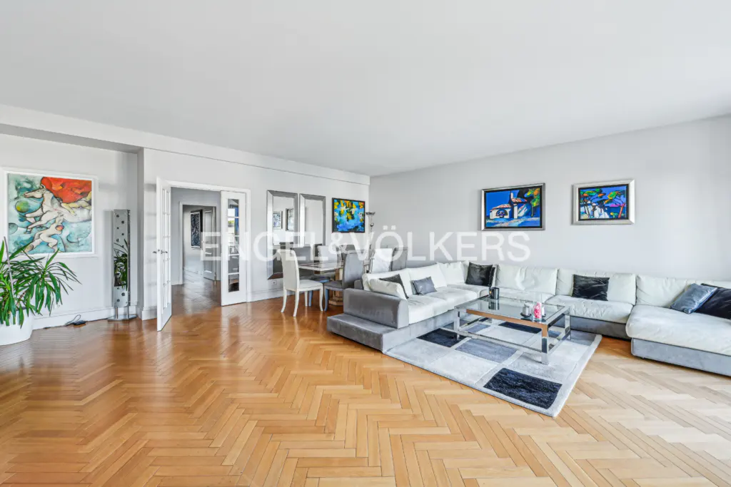 A wide shot of a living room with hardwood floors, a white sectional sofa, and colorful artwork.