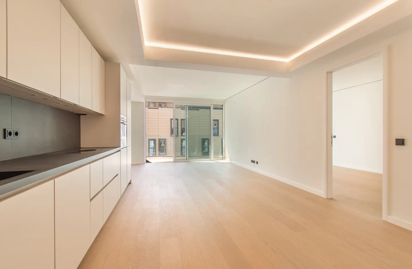 Bright, modern apartment interior with white cabinets, light wood floors, and a sliding glass door to a balcony.