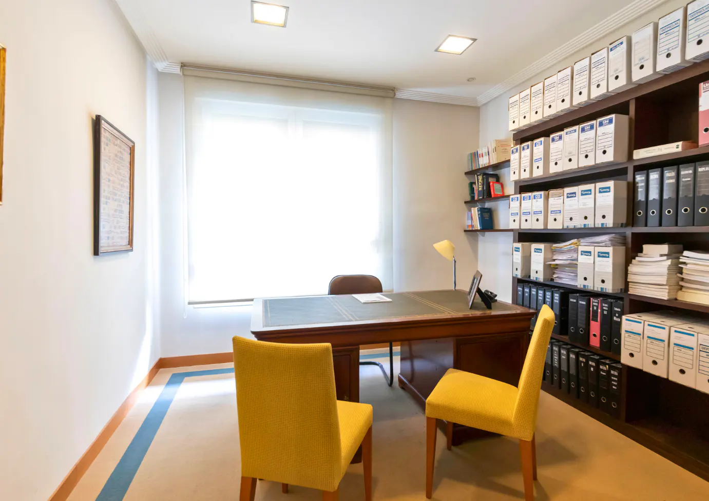 Office with a large wooden desk, yellow chairs, and floor-to-ceiling shelves filled with binders and books.