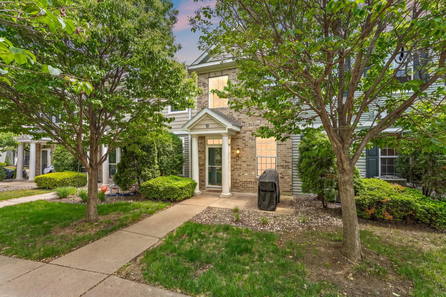 Exterior view of a two-story townhouse with brick and siding, a covered porch, and a grill on the patio.