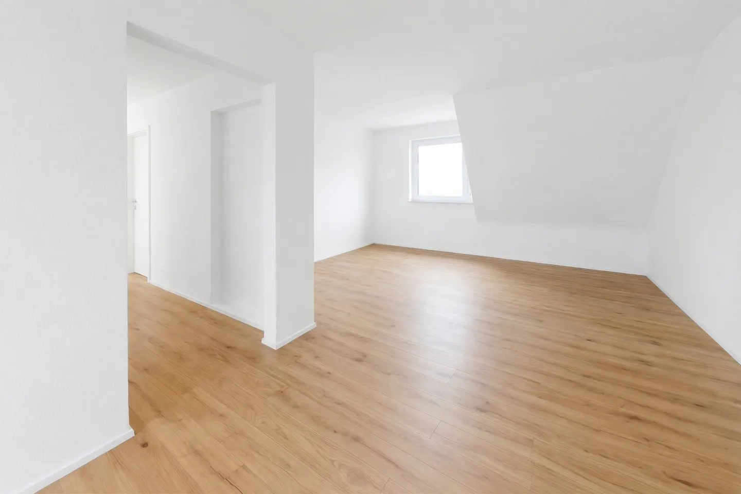 Bright, empty room with light wood floors and white walls. A window lets in natural light. A doorway leads to another room.