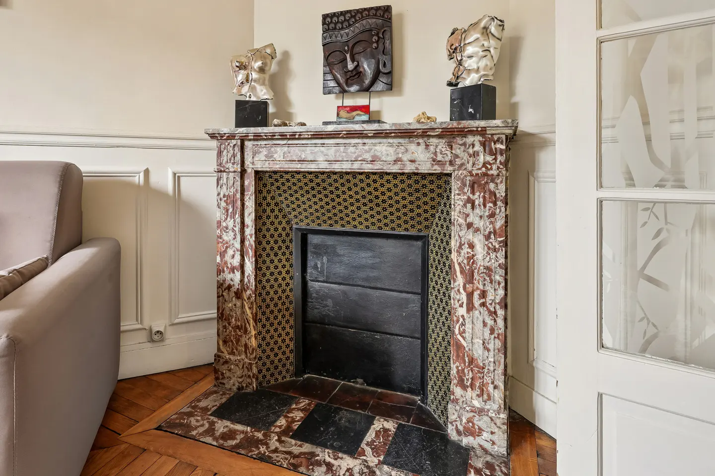 Living room with a marble fireplace topped with sculptures, a black Buddha head, and a beige sofa.