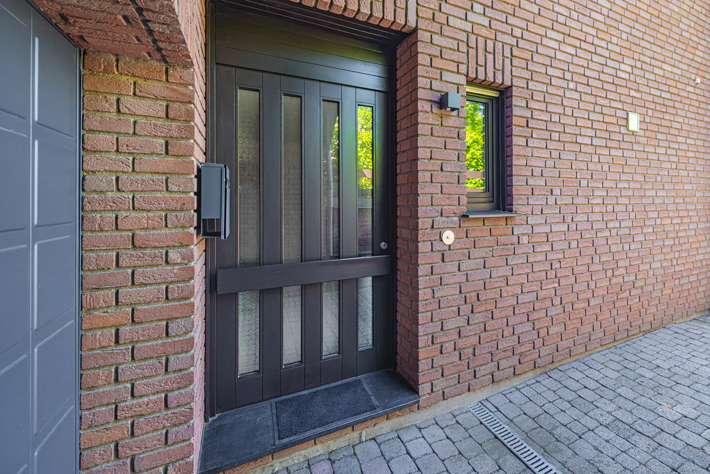 Exterior shot of a brick house with a dark brown front door with glass panels and a small window.