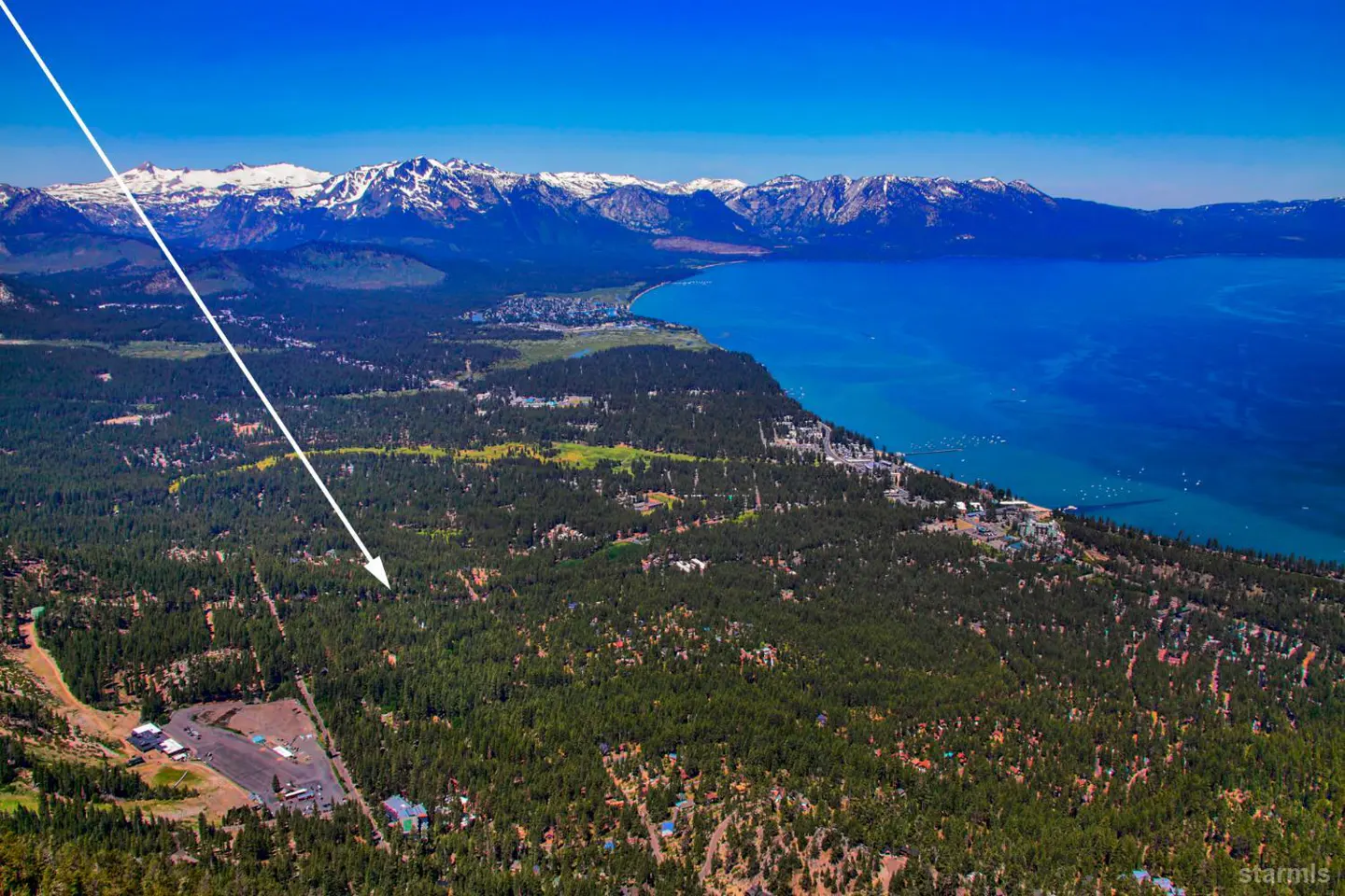 Aerial view of Lake Tahoe with snow-capped mountains, green forest, and an arrow pointing to a property.