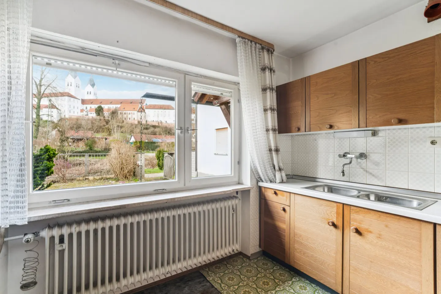A kitchen with wood cabinets, a white tiled backsplash, and a window view of a large building.