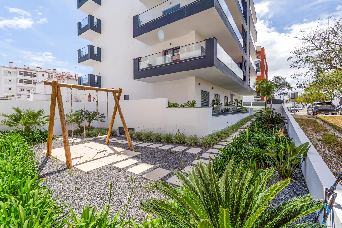 Modern white apartment building with black trim, a wooden swing set, and lush green landscaping.