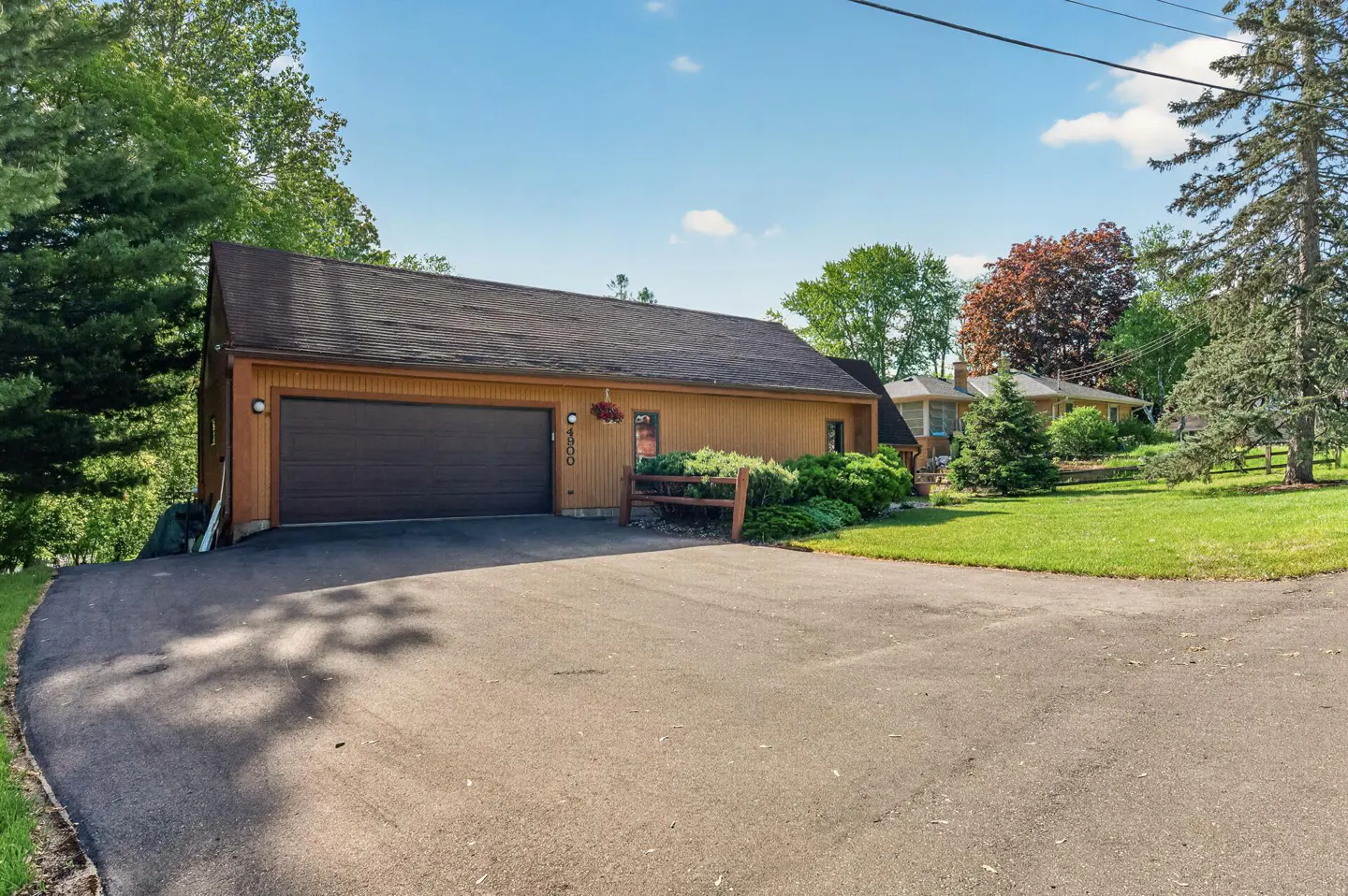Exterior view of a tan house with a dark brown garage door and roof, green lawn, and blue sky.