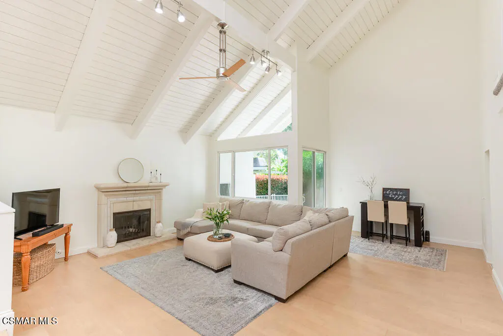Bright living room with vaulted ceilings, a stone fireplace, and a beige sectional sofa on a gray rug.