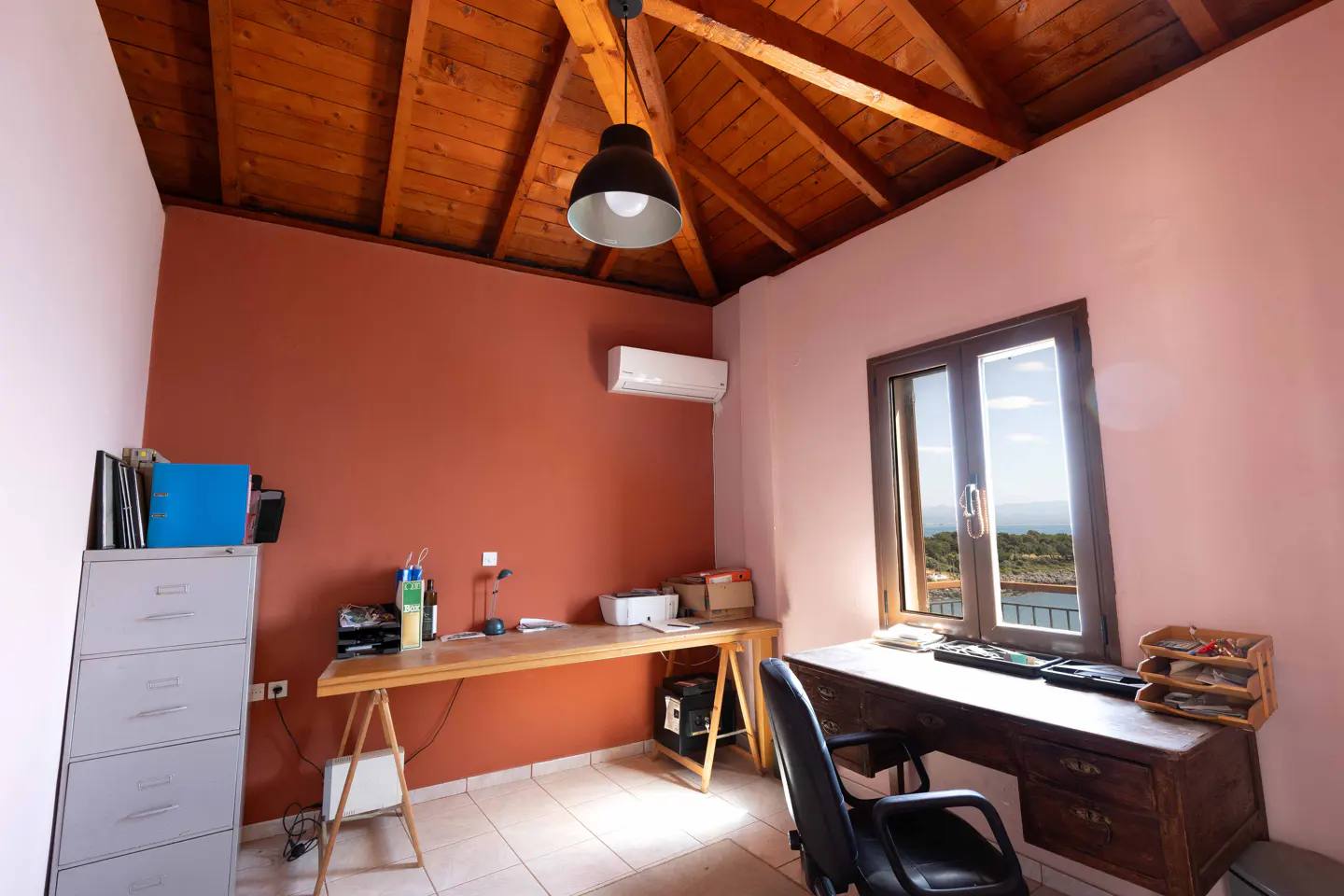 A home office with a wooden ceiling, two desks, a filing cabinet, and a window with a view.