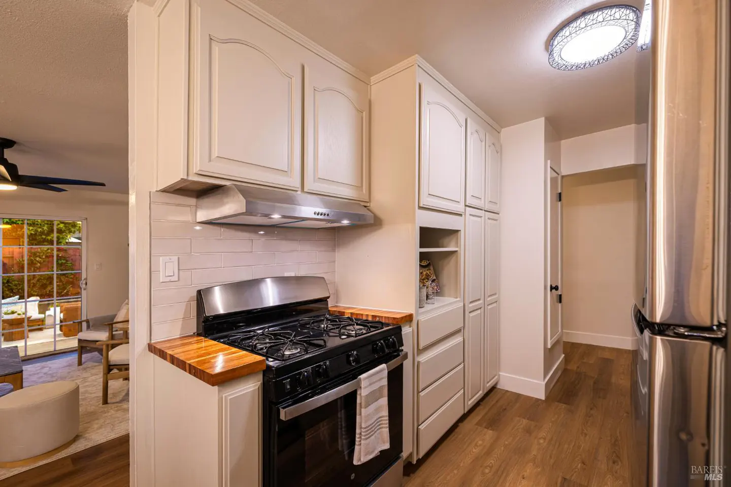 A kitchen with cream cabinets, a black stove, and wood countertops. A stainless steel refrigerator is on the right. Wood floors run throughout.