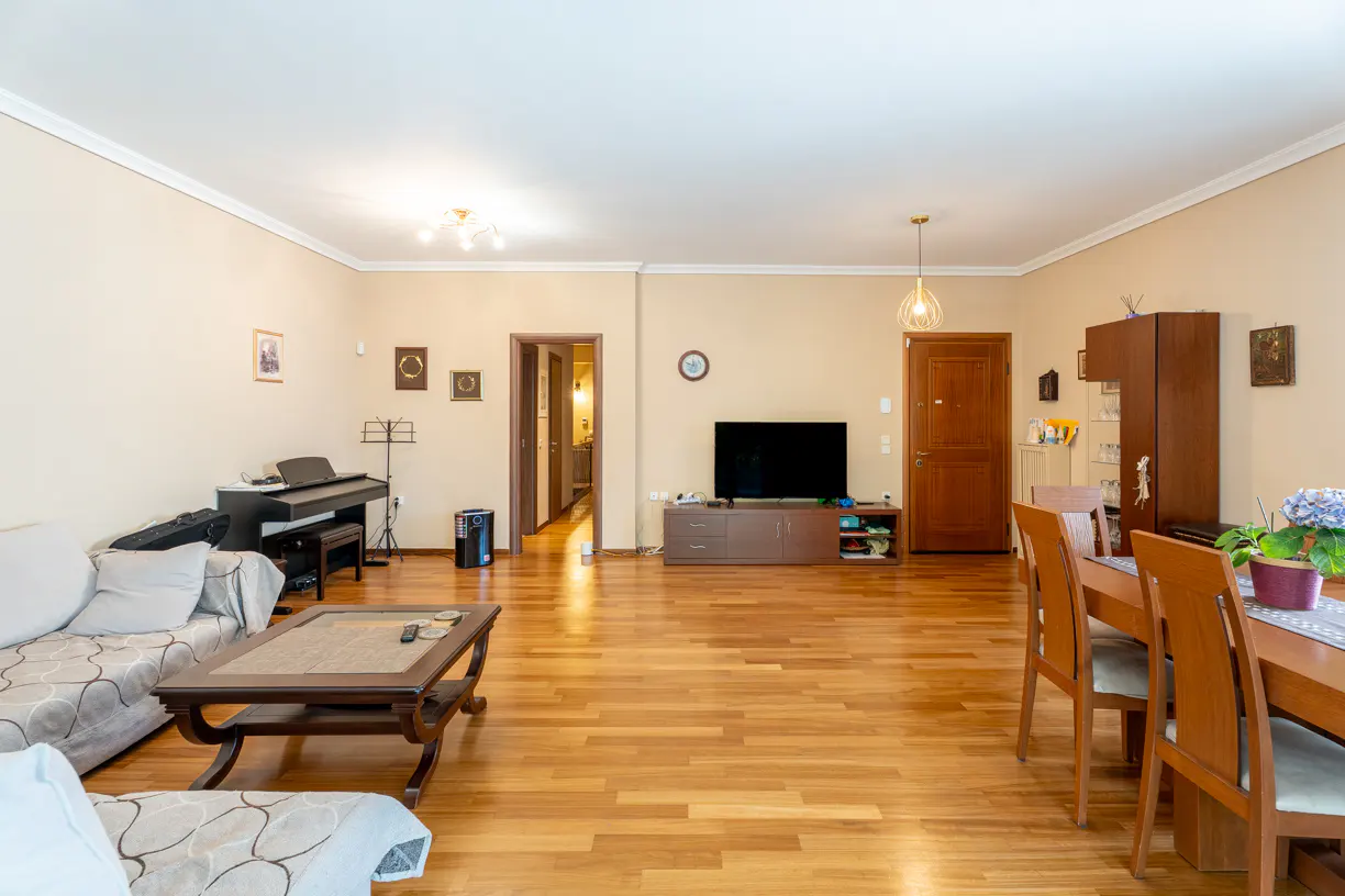 A wide shot of a living room with a piano, sofa, TV, and dining table on a wooden floor.