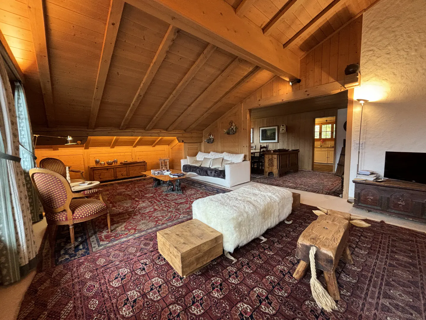Cozy attic living room with wood-paneled ceiling, white sofa, patterned rug, and rustic wooden furniture.